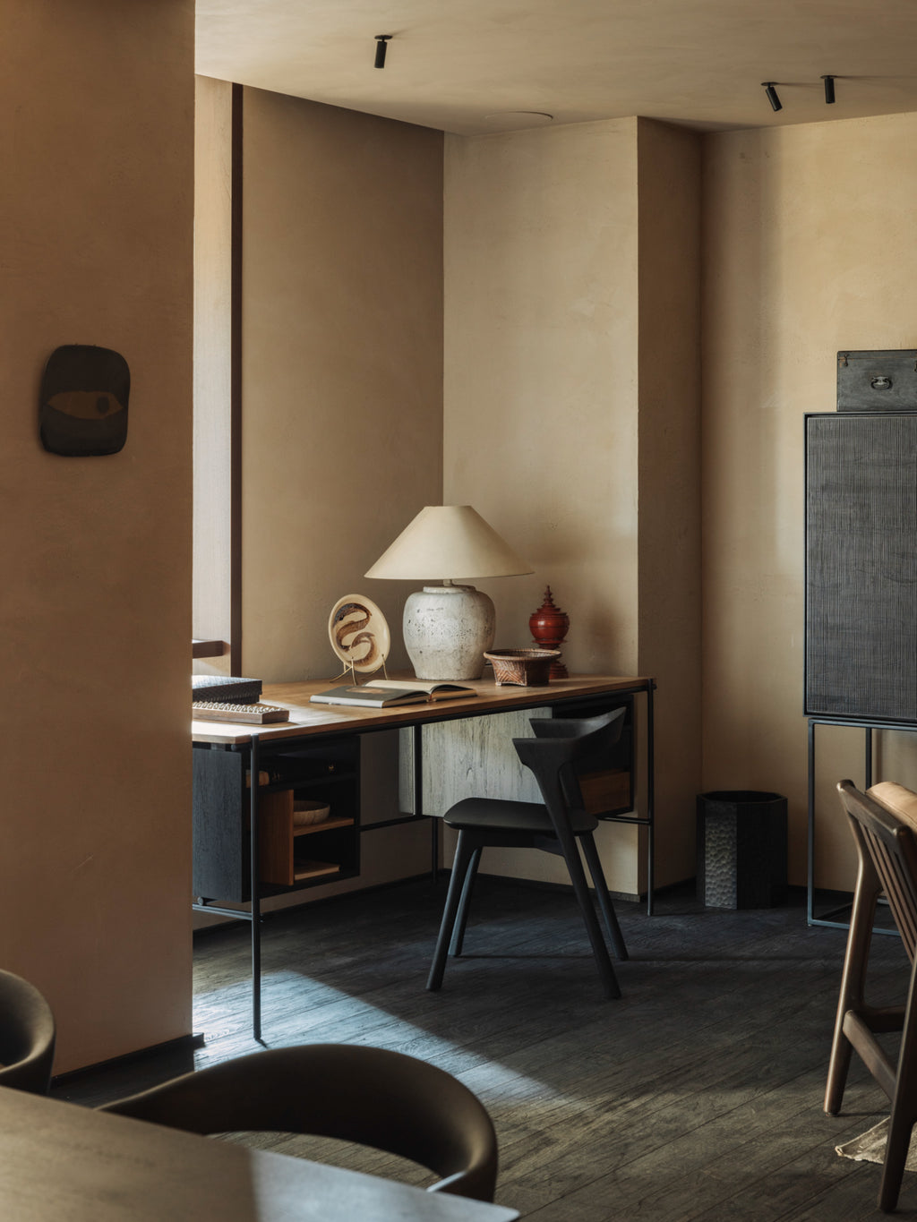 Ethnicraft Oscar Desk, a modern wooden desk with sleek black metal legs, paired with a black chair, and adorned with a ceramic lamp and decorative items in a warm, inviting room.
