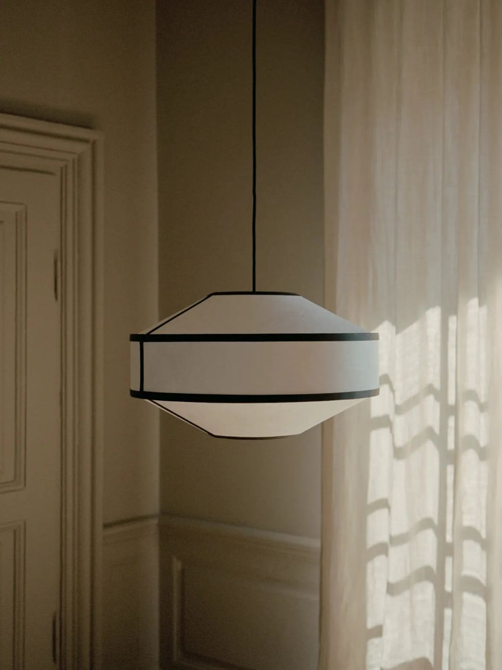 New Works Kite Pendant Lamp featuring a luxury cream fabric shade with subtle black trim, hanging artfully in a sunlit room. Perfect for modern interior design.