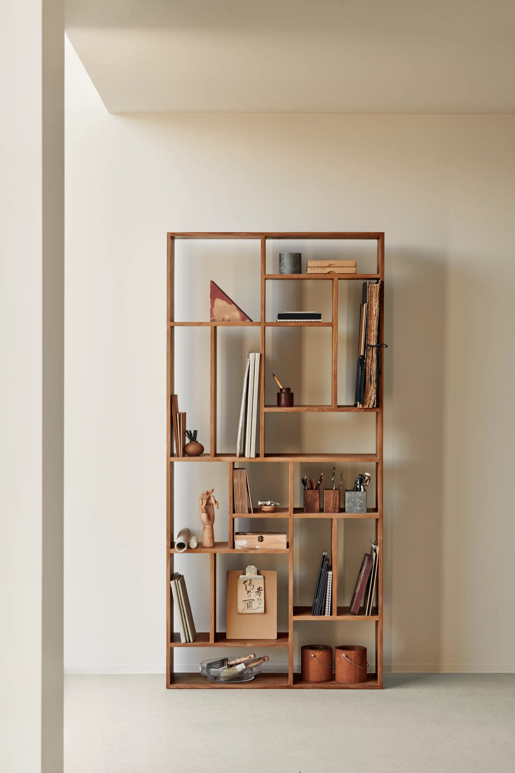Ethnicraft M Rack, a striking modern minimalist shelving unit crafted from rich solid teak wood with a warm brown finish and smooth texture. This contemporary bookcase features a unique asymmetrical, open-back geometric design, offering versatile display spaces for books and decorative objects. It's an ideal statement piece for a living room, home office, or as an elegant room divider in Japandi or Scandinavian-inspired interiors.