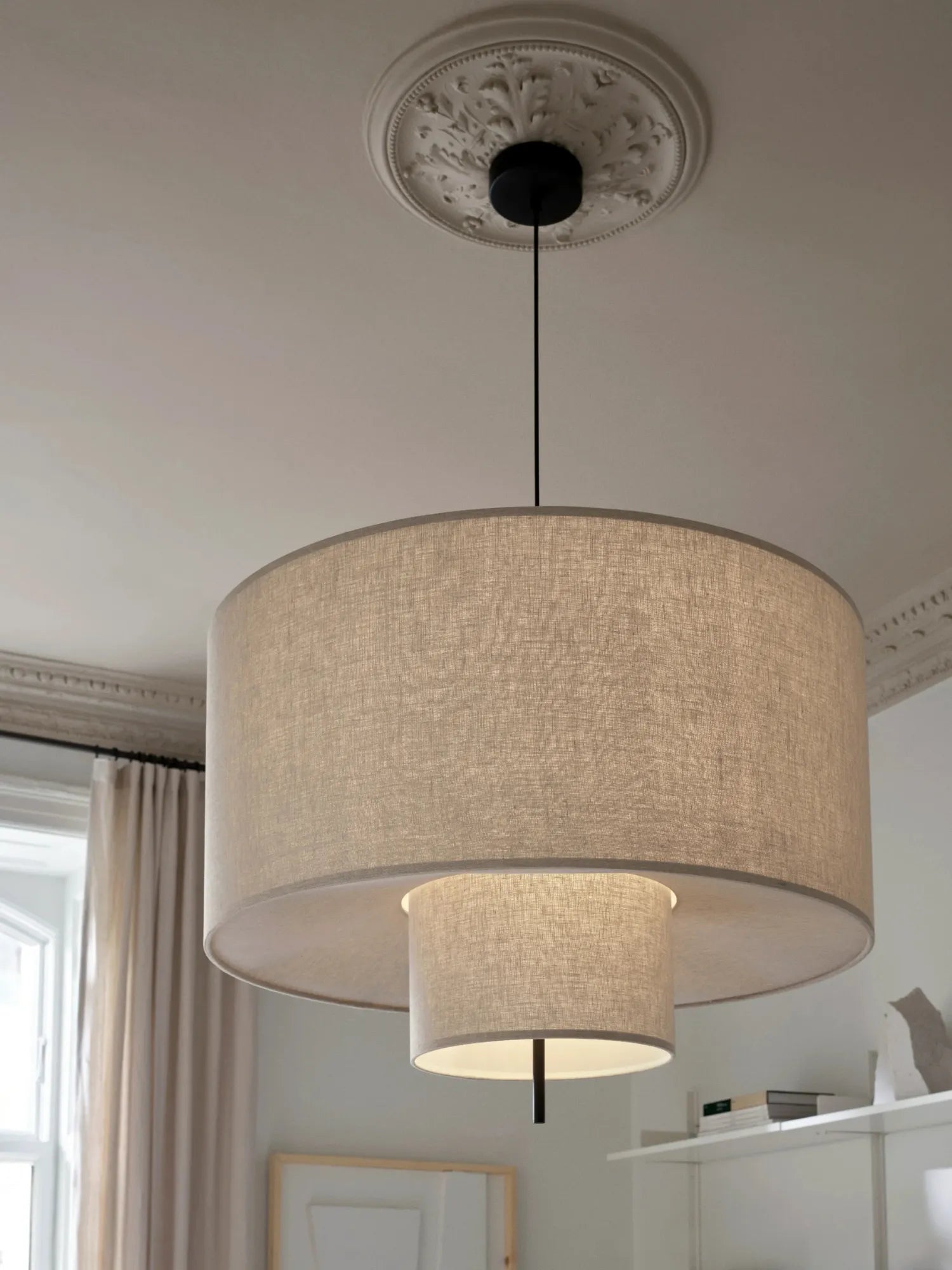 New Works Margin Pendant Lamp, a layered drum shade fixture with a large outer natural linen shade and smaller inner linen shade, illuminated from within. This luxury lighting solution provides soft, ambient light.
