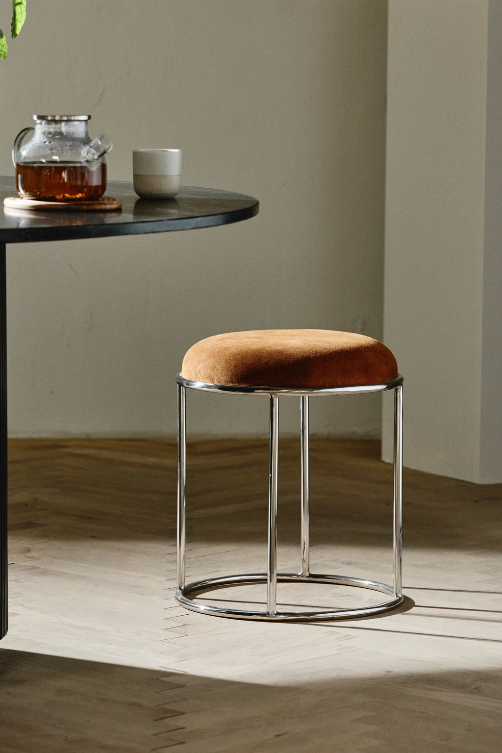Nordal Komati Stool, a sleek modern minimalist stool featuring a plush round seat upholstered in a rich cognac brown suede-like fabric, supported by a polished chrome-plated metal frame with clean, tubular lines and a circular base. This contemporary accent stool is perfect for living rooms, bedrooms, or as a chic vanity seat in Nordic or industrial chic interiors.