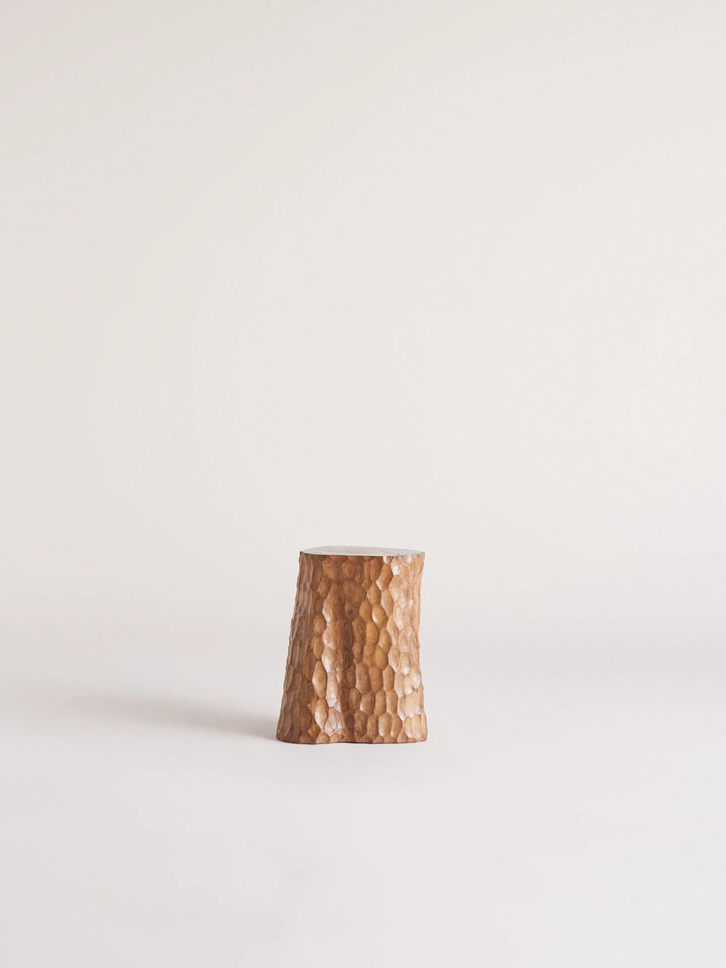 Heaps & Woods Clara Stool, a solid wood accent stool featuring a rich, warm brown finish and a unique hand-carved, dimpled texture across its tapered, drum-like silhouette. This organic modern side table is crafted from natural wood, showcasing artisanal detail and a rustic charm. Ideal for adding a natural element as a bedside table, living room accent, or small side table in wabi-sabi or contemporary spaces.
