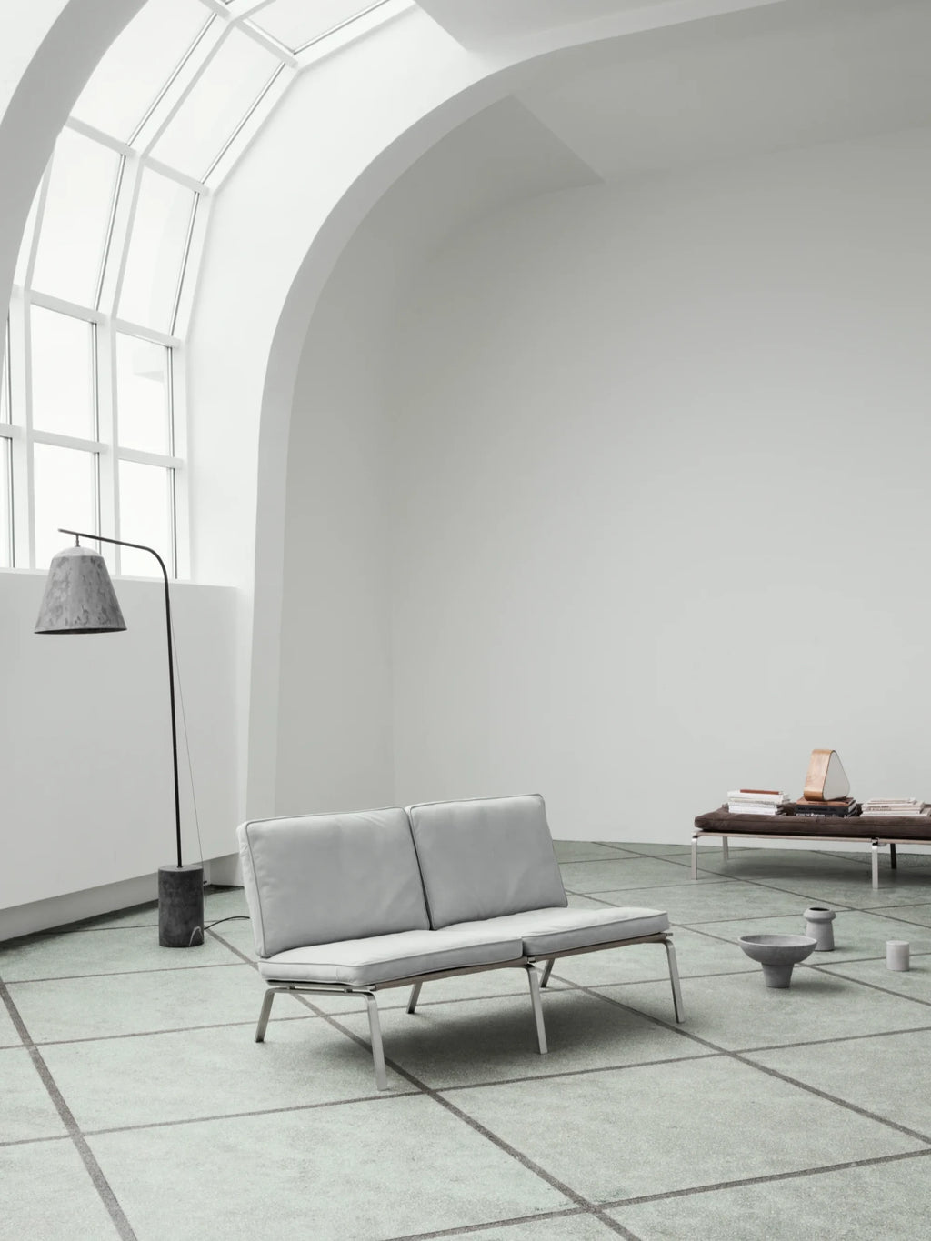 NORR11 Man 2 Seater Sofa, a sleek modern minimalist sofa featuring plush light grey fabric cushions with refined piping details, supported by a low-profile metallic silver frame. This contemporary 2-seater sofa offers clean Scandinavian lines and a sophisticated aesthetic. Ideal for modern living rooms, apartment lounge areas, or a stylish home office.