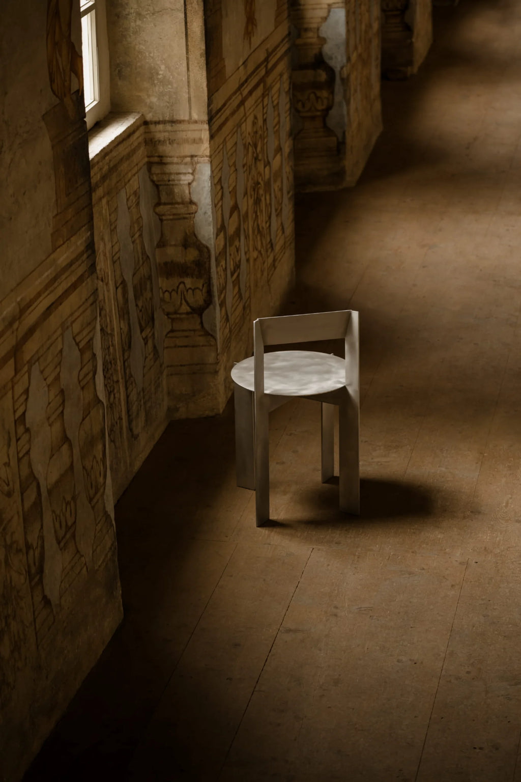 NG DESIGN Object 111 Chair, a minimalist silver metallic chair with a flat round seat & rectangular base, shown from above in a moody room with antique painted walls. A premium architectural statement piece.