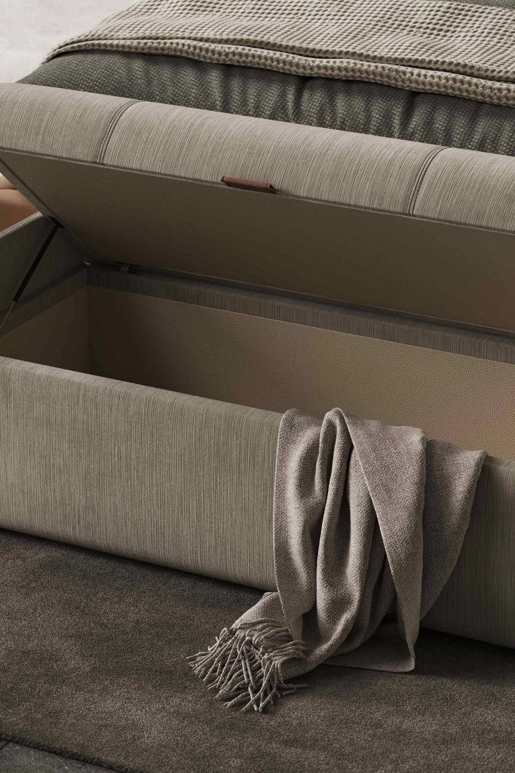 Domkapa Adley Bench, a modern minimalist storage bench upholstered in a textured greige fabric with subtle vertical ribbing. This contemporary design features a hinged lift-top lid, revealing generous interior storage lined with a rich dark tan faux leather, and accented with a sleek dark brown leather pull tab. Ideal as an end of bed bench for bedroom storage or a stylish entryway bench in organic modern and minimalist homes.