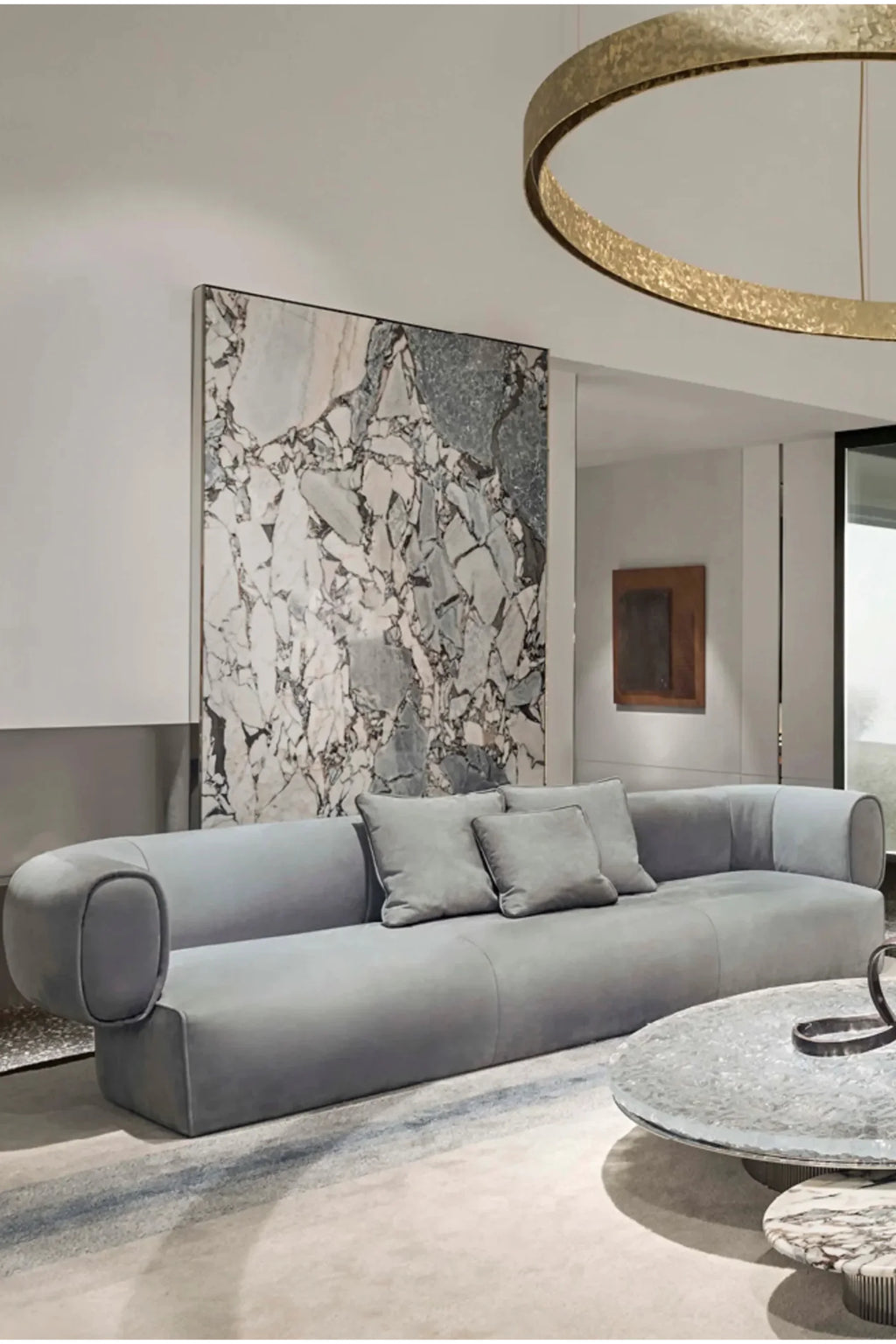 Hessentia Hug Sofa, a contemporary organic modern sofa upholstered in soft dove grey fabric with a distinctive curved silhouette and plush, rounded armrests and backrest. This luxury fabric sofa features a sleek, minimalist profile, complemented by matching grey throw pillows. Ideal for a sophisticated living room, modern lounge seating, or a contemporary open-plan space.