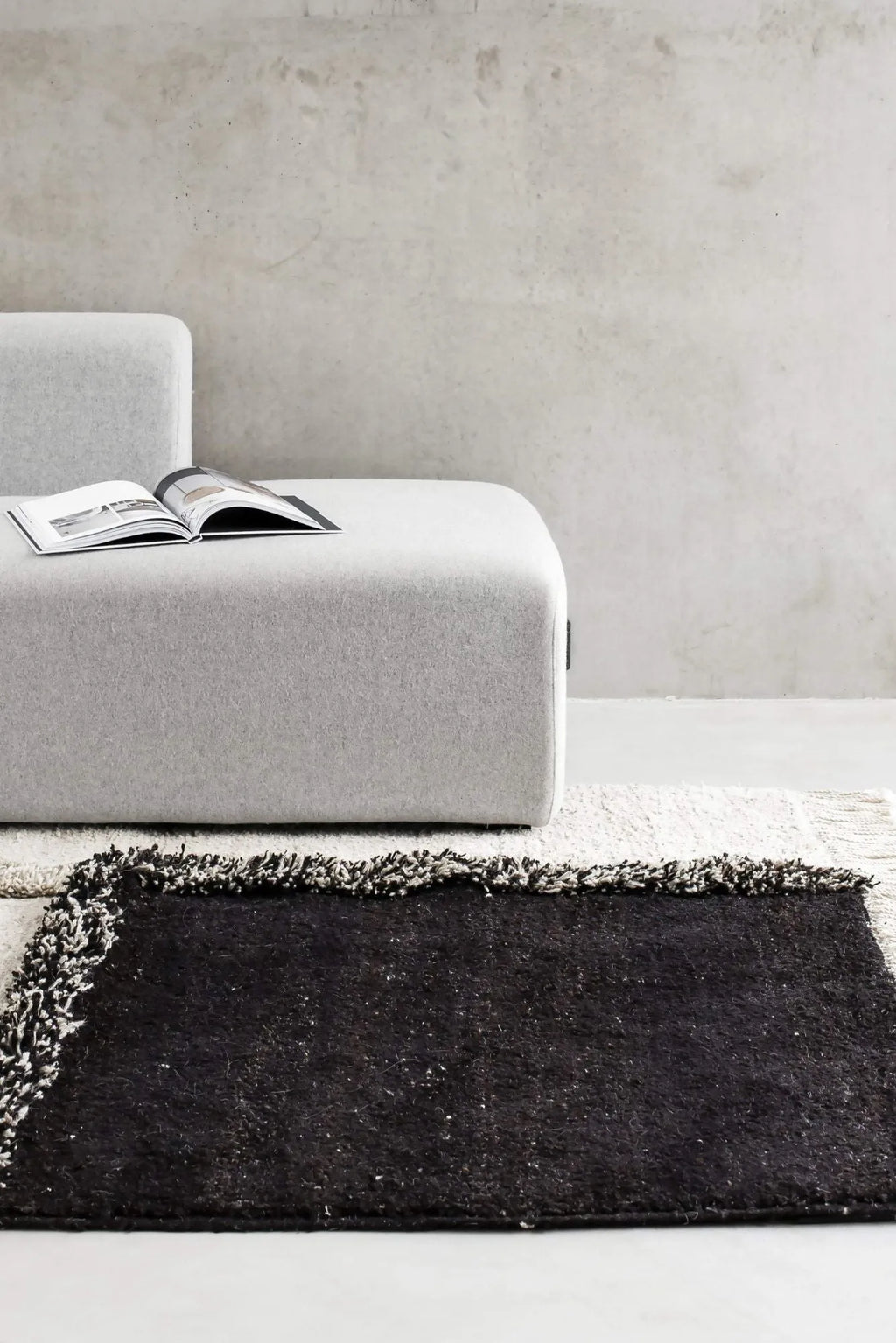 Sera Helsinki E-1027 Wool Rug, a rectangular black wool area rug featuring a dense, shaggy high pile texture and contrasting white and grey fringed edges. This hand-knotted wool rug offers a cozy yet sophisticated grounding element for modern minimalist, Scandinavian, or industrial living rooms and bedrooms.