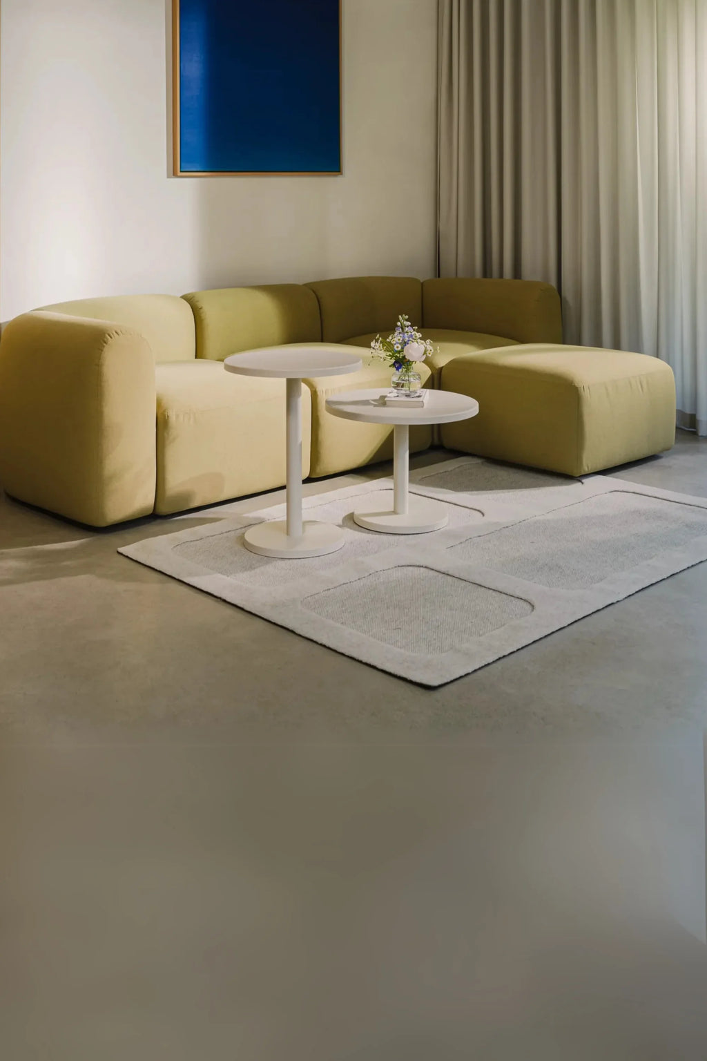 noo.ma Flom Corner Sofa, a contemporary modular L-shaped sofa upholstered in a soft pale olive green fabric, featuring a low-profile design with plump, rounded cushions and deep seating for ultimate comfort. This organic modern sectional offers a versatile configuration, perfect for creating a cozy and stylish living room centerpiece in minimalist or Scandinavian-inspired homes.