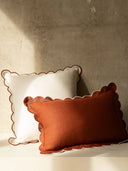 Two decorative pillows, one white and one orange, on a neutral background