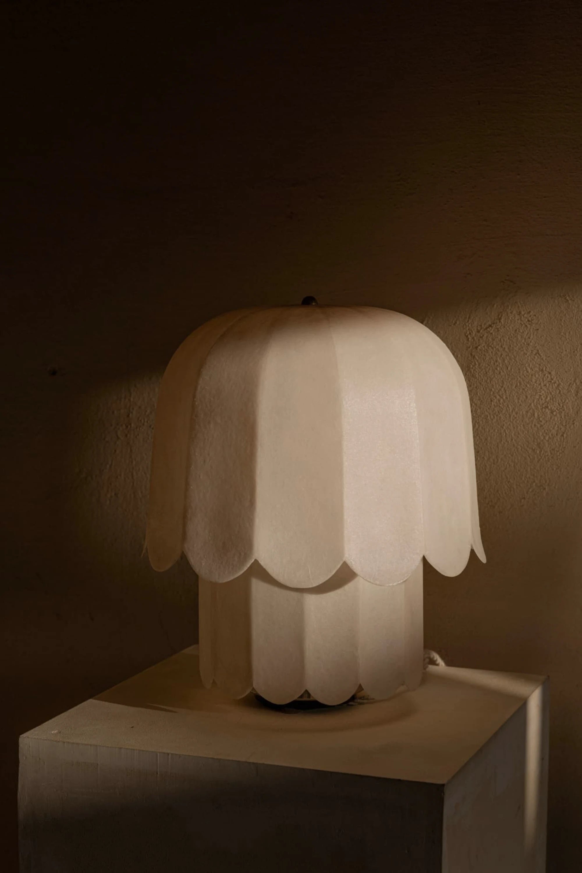 Kilzi white feather table lamp on a concrete pedestal surface with a moody background