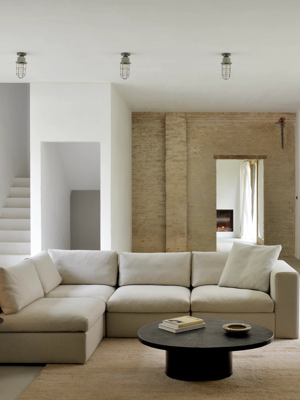 Ethnicraft Slice Coffee Table, a round, dark-finished table with a textured surface, positioned in front of a large, light-colored sectional sofa. The modern, minimalist design complements the spacious, contemporary living area.