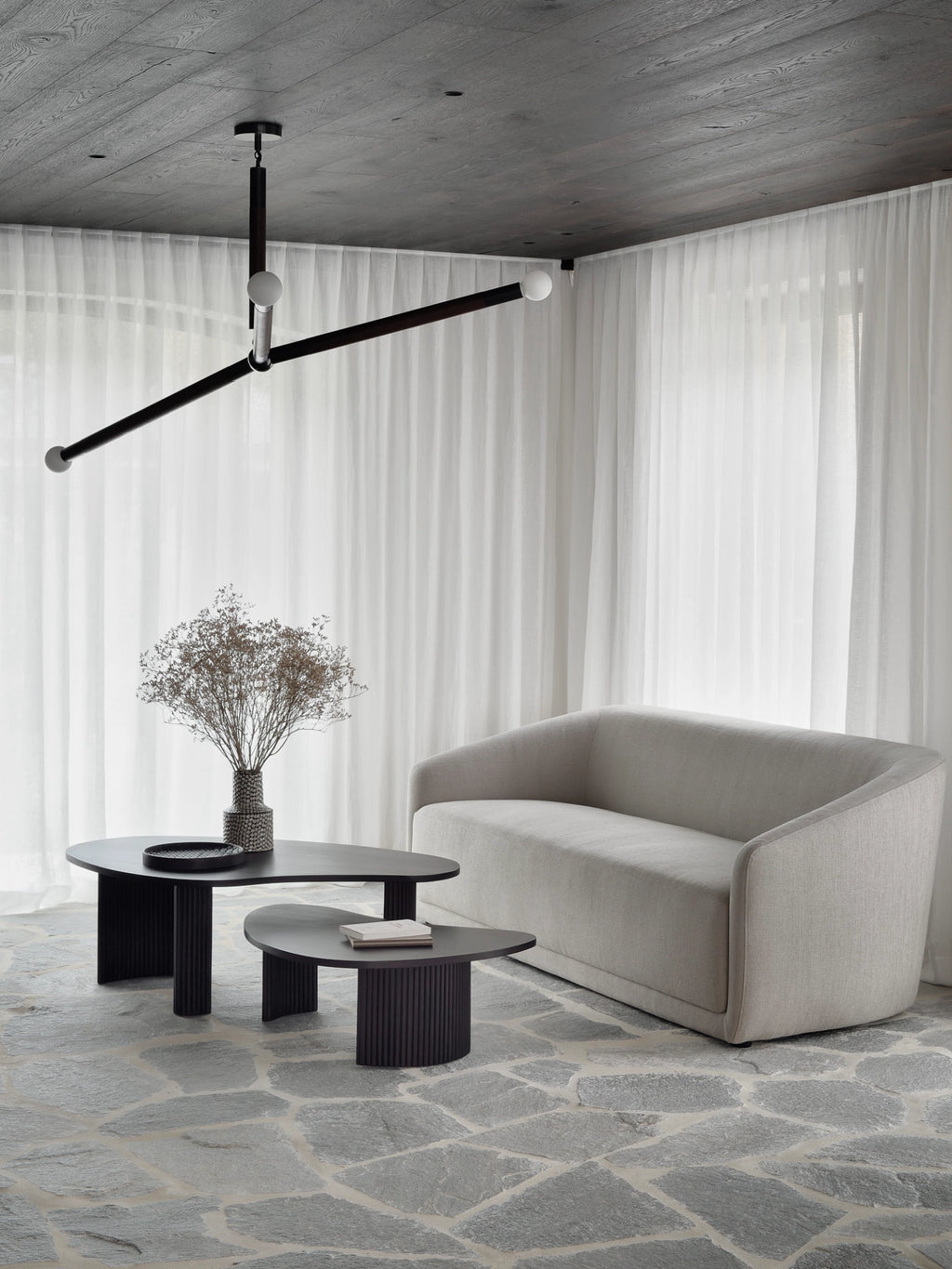 Ethnicraft Boomerang Coffee Table set, two dark mahogany tables with distinct curved tops and slatted bases, elegantly placed in a bright, minimalist living space with a light beige sofa and sheer curtains.