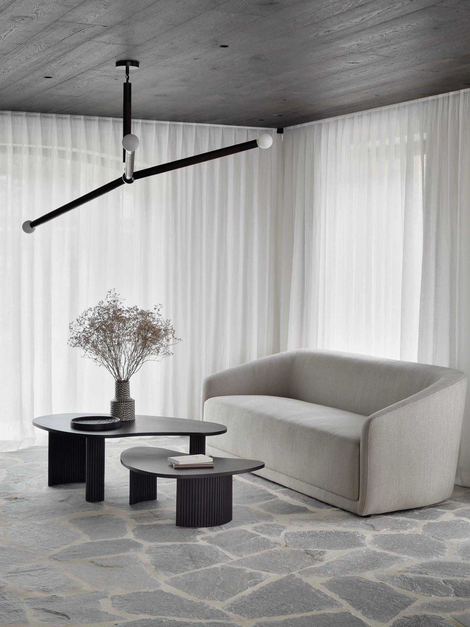 Ethnicraft Boomerang Coffee Table set, two dark mahogany tables with distinct curved tops and slatted bases, elegantly placed in a bright, minimalist living space with a light beige sofa and sheer curtains.