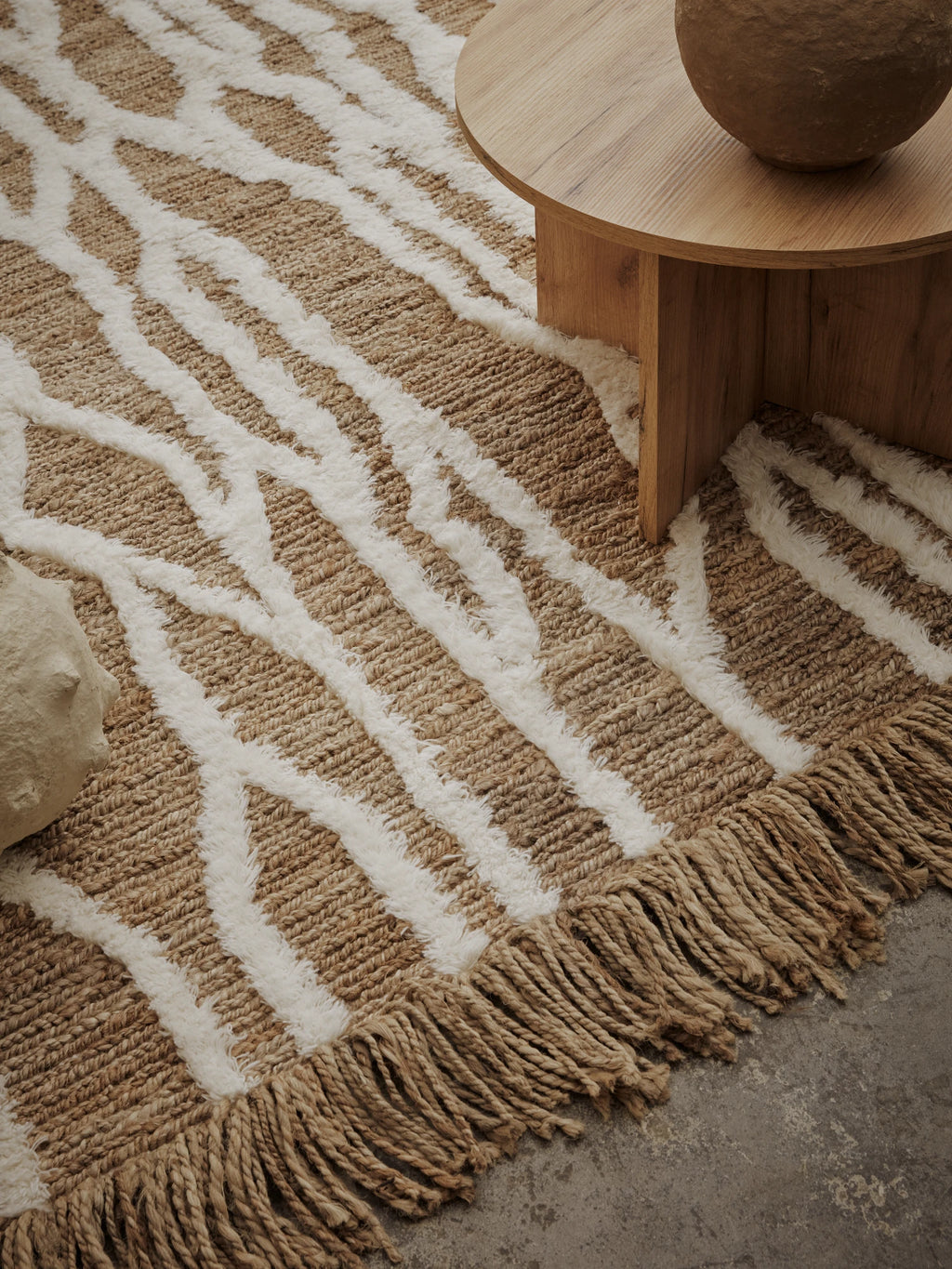 Tinted Objects Wahl Jute Rug, featuring a natural light brown woven jute base with thick, raised cream white abstract patterns and braided fringe edges. This durable, eco-friendly area rug is perfect for adding bohemian texture and warmth to a modern living room or bedroom.