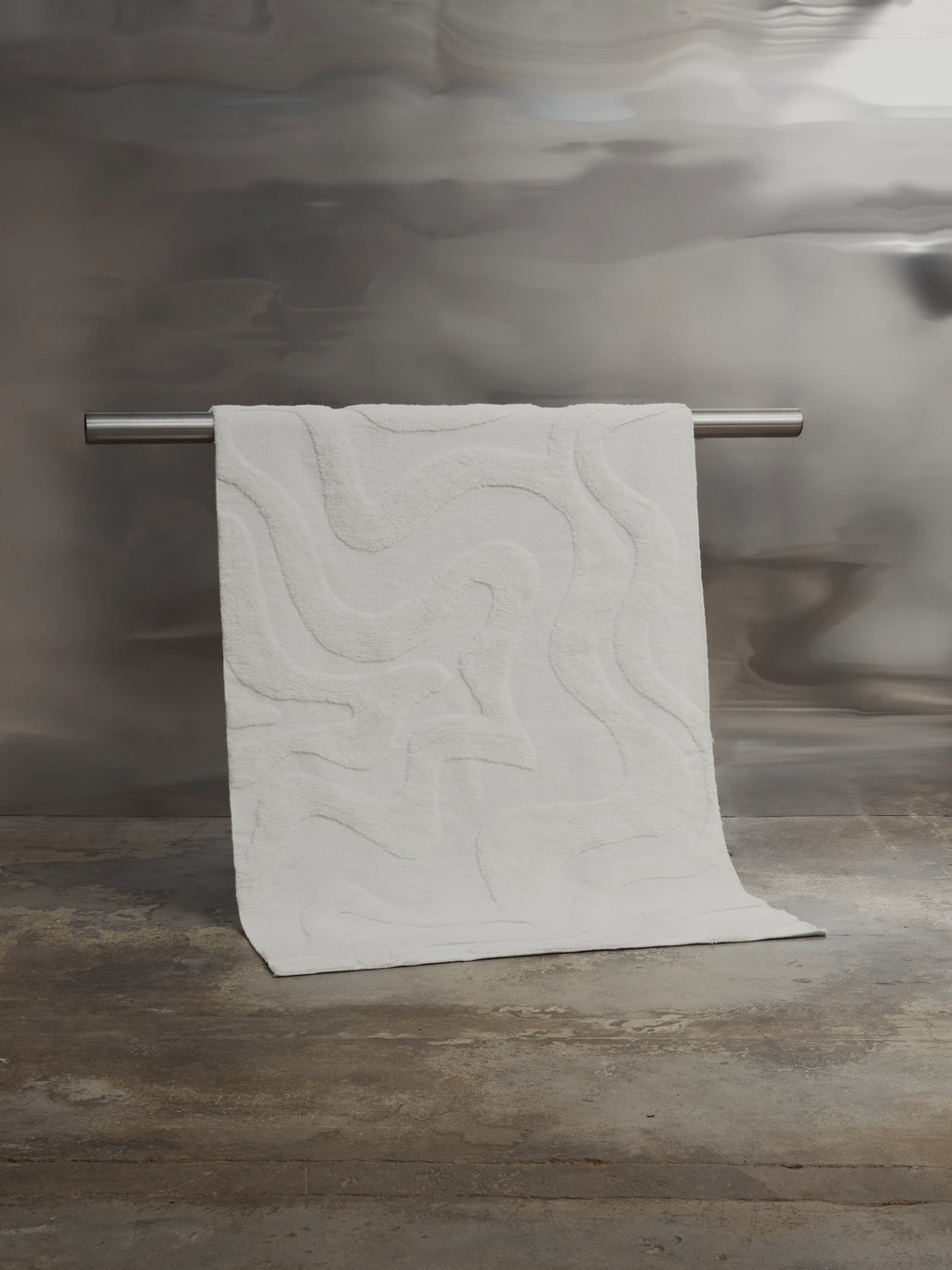 Tinted Objects Norlander Wool Rug, a plush off-white modern area rug with an abstract raised wavy pattern, draped over a silver metal bar. This luxurious and soft wool rug is perfect for adding contemporary style and comfort to any stylish living space or bedroom.