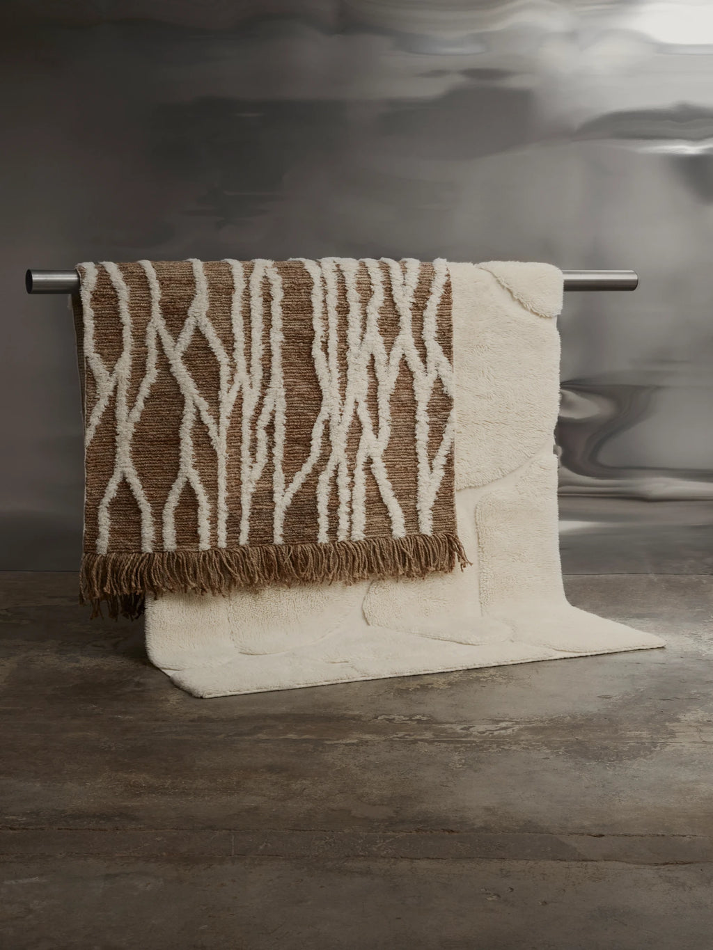 Tinted Objects Wahl Jute Rug, featuring a natural brown woven base with an abstract white pattern and fringed edges, draped over a plush cream-colored rug. This stylish and durable area rug is perfect for adding natural texture and a bohemian touch to any modern living space or bedroom.