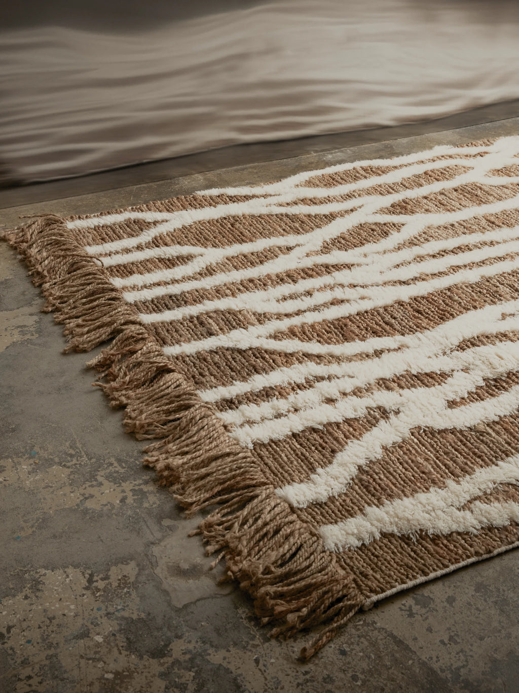 Tinted Objects Wahl Jute Rug, a durable natural fiber rug featuring a woven brown and cream zebra print pattern with textured shag accents and braided fringe. This stylish accent rug is perfect for adding bohemian warmth and texture to modern living rooms or bedrooms.