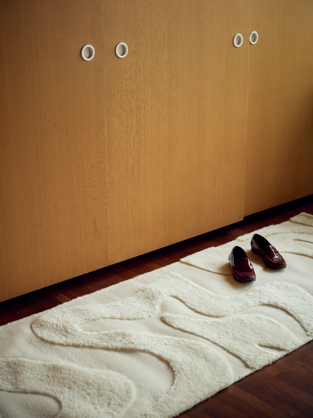 Tinted Objects Norlander Wool Runner Rug, a luxurious cream-colored rug with a raised, organic wavy pattern, laid on dark hardwood flooring. This premium wool runner provides a stylish and soft accent for hallways or entryways in modern homes.