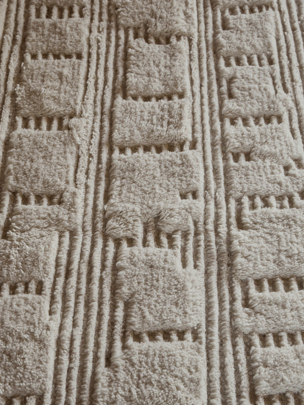 Tinted Objects Lydahl Handknotted Rug, featuring a plush, textured cream-colored pile with raised square patterns and linear grooves, creating a modern geometric design. This luxurious area rug is perfect for adding warmth and sophisticated style to contemporary living spaces and bedrooms.