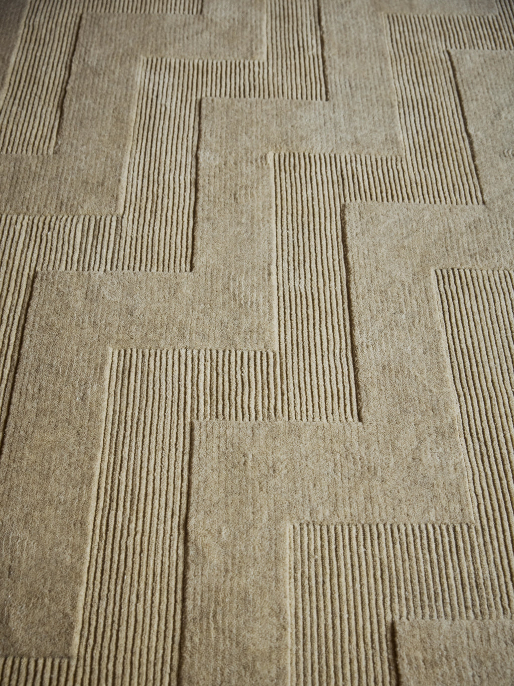 Tinted Objects Valmont Wool Rug, featuring a modern geometric maze pattern in natural beige wool with textured raised lines and soft flat pile sections. This elegant area rug adds warmth and contemporary style to any living room or bedroom for design-conscious homeowners.