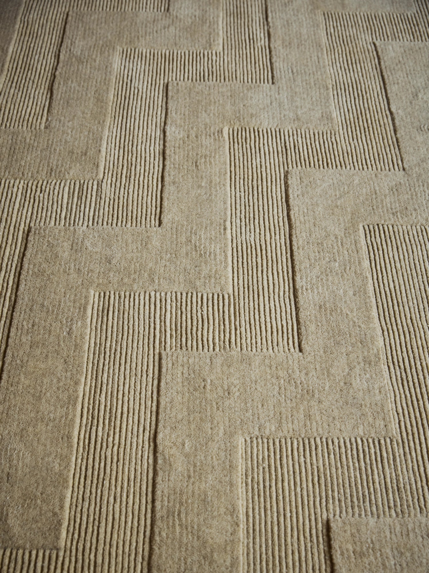 Tinted Objects Valmont Wool Rug, featuring a modern geometric maze pattern in natural beige wool with textured raised lines and soft flat pile sections. This elegant area rug adds warmth and contemporary style to any living room or bedroom for design-conscious homeowners.