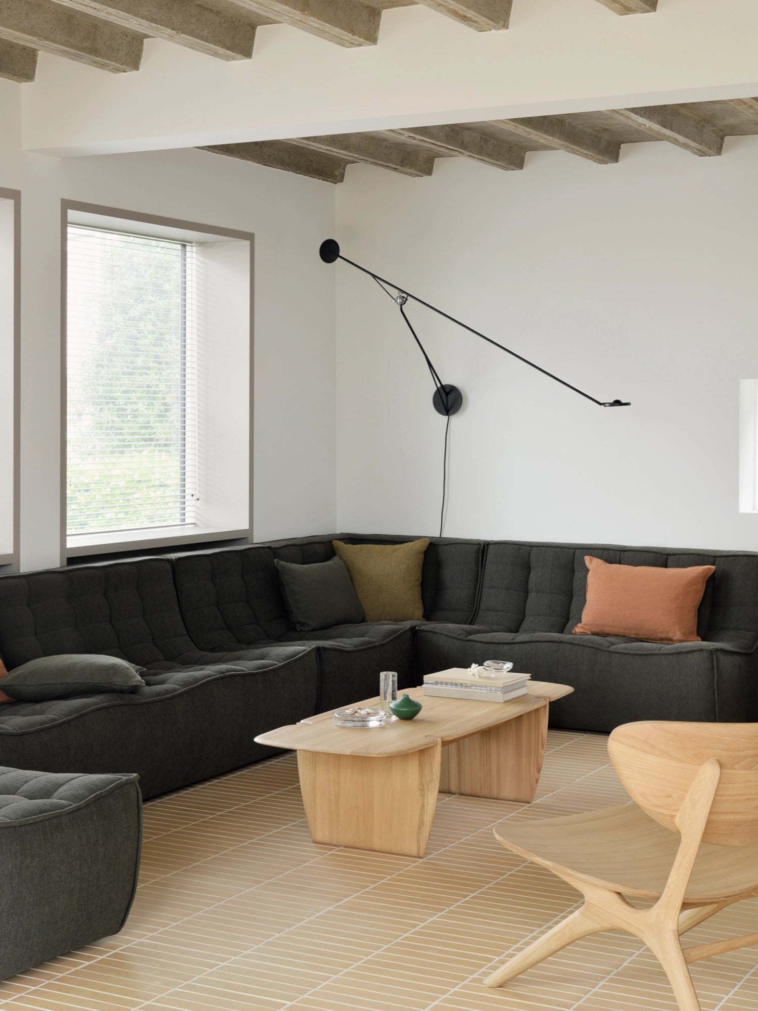 Ethnicraft PI Coffee Table, a light-colored wooden coffee table with a natural grain and unique, sculpted base, centrally placed in a modern living room with a dark grey sectional sofa.