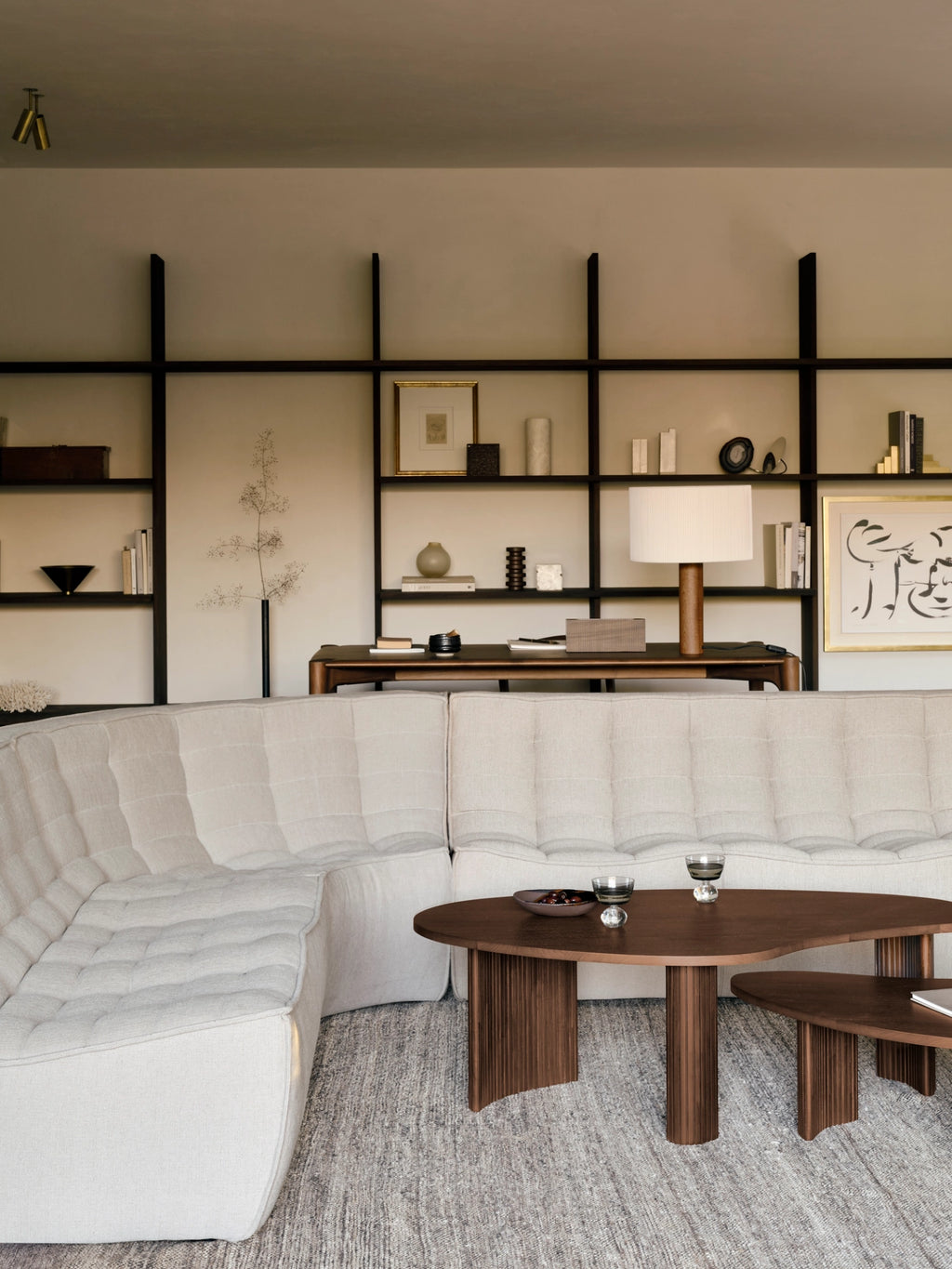 Ethnicraft Boomerang Coffee Table set in a contemporary living room, featuring two dark brown mahogany tables with unique curved shapes, complementing a light-colored sectional sofa and modern decor.