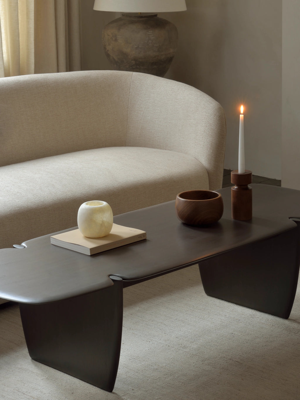 Ethnicraft PI Coffee Table, a close-up of the dark brown rectangular wooden coffee table, showcasing its smooth finish and distinctive curved base, adorned with a candle and decorative bowl.