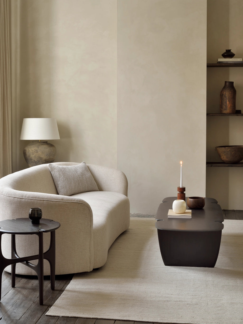 Ethnicraft PI Coffee Table, a dark brown rectangular wooden coffee table with a unique, organic shape and robust base, placed on a light rug in a cozy living area with a curved cream sofa.