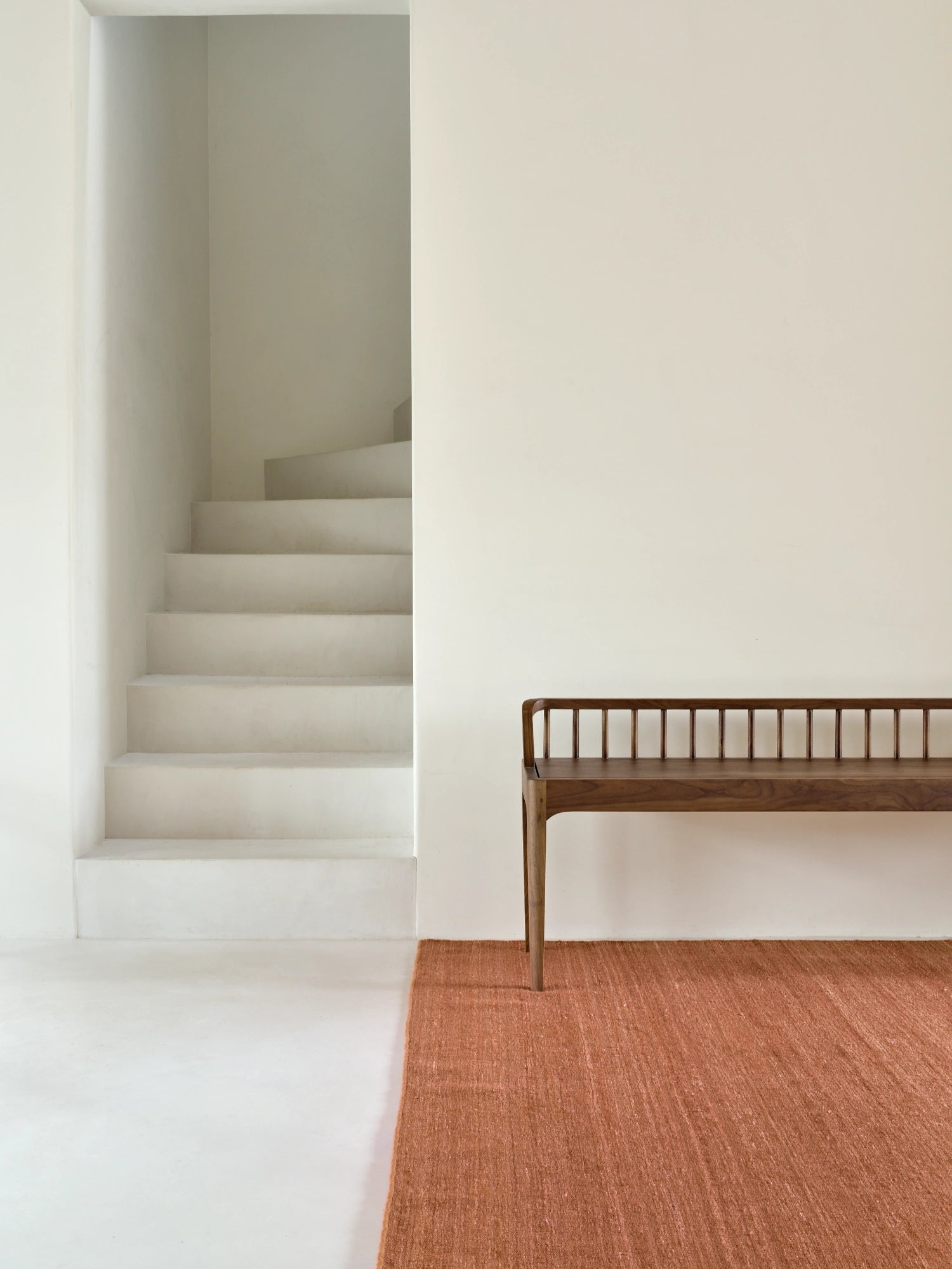 Ethnicraft Spindle Bench, a modern minimalist bench crafted from solid dark walnut wood, featuring a slatted spindle backrest with a gracefully curved top rail, a rectangular seat, and sleek tapered legs. This Scandinavian-inspired wooden bench is perfect for an entryway, hallway, or as a stylish dining bench for contemporary interiors.