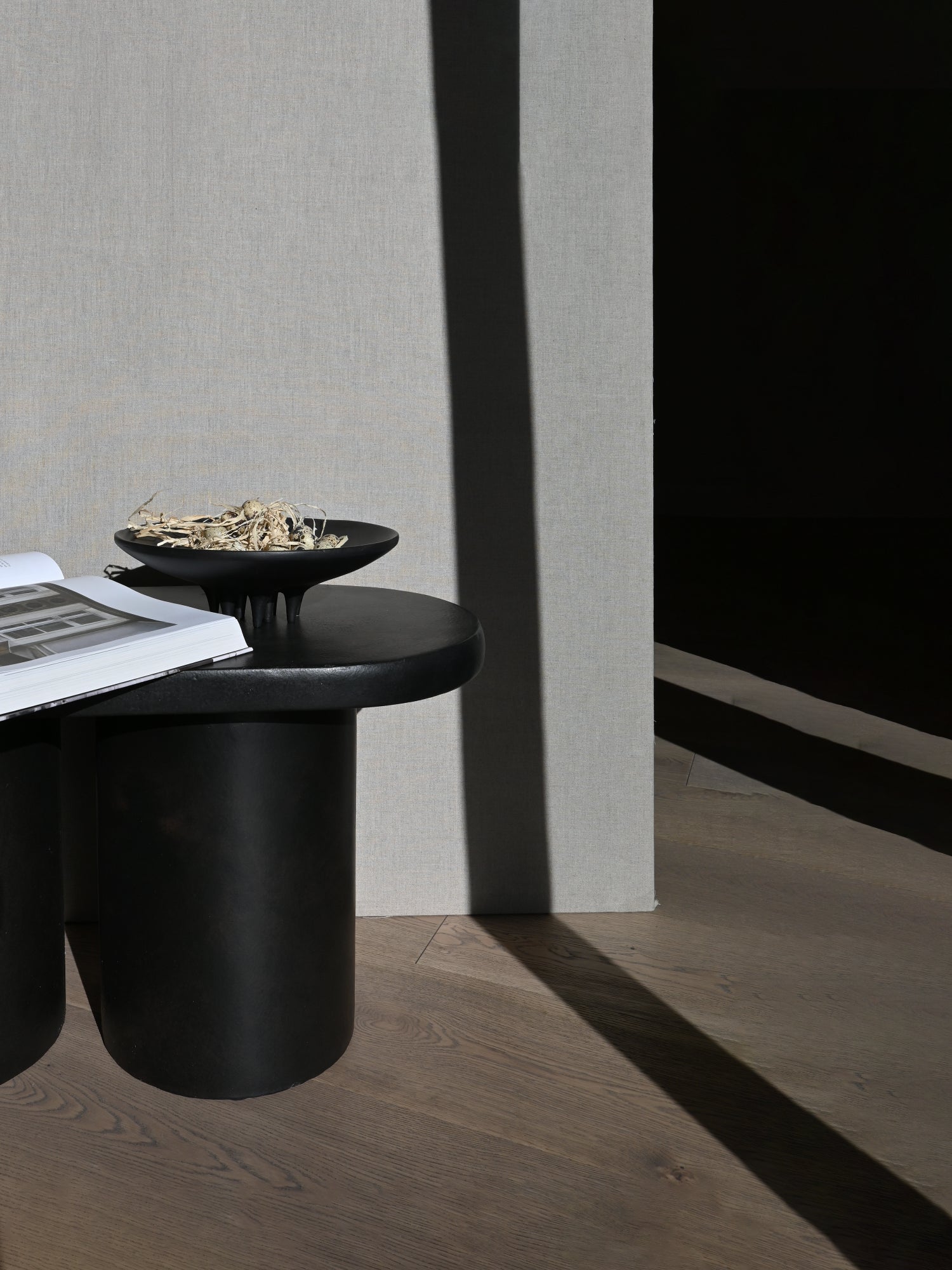 101 CPH Medusa Tray, a deep black, subtly textured premium ceramic bowl with three distinctive stubby legs, filled with dried botanicals, sitting on a dark side table with an open book. Ideal for a modern decor accent.