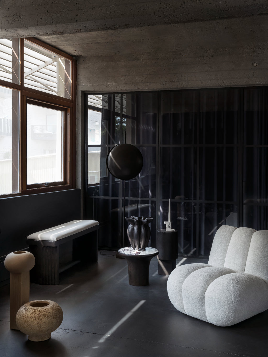 101 CPH Totem Floor Lamp with a matte black, spherical shade and minimalist bronze stand, positioned next to a chic, white bouclé armchair in a modern living space. This sculptural, luxury lighting piece adds sophisticated ambiance.