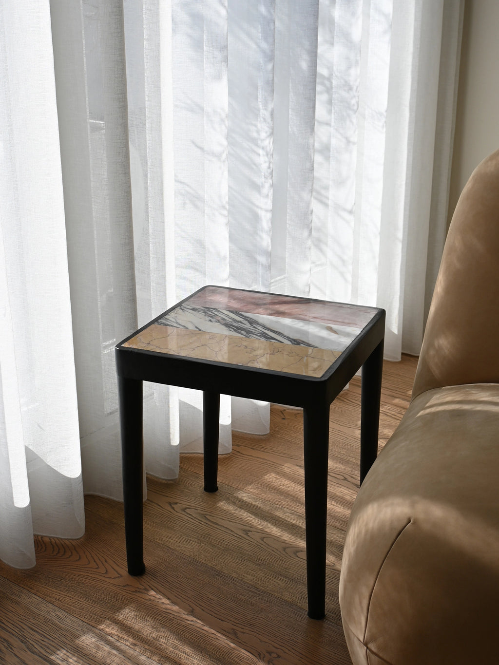 101 CPH Tairu Table: A premium square end table with a multicolored marble top featuring white, grey, beige, and pink strips, and a sleek black metal frame. Ideal for modern living spaces.