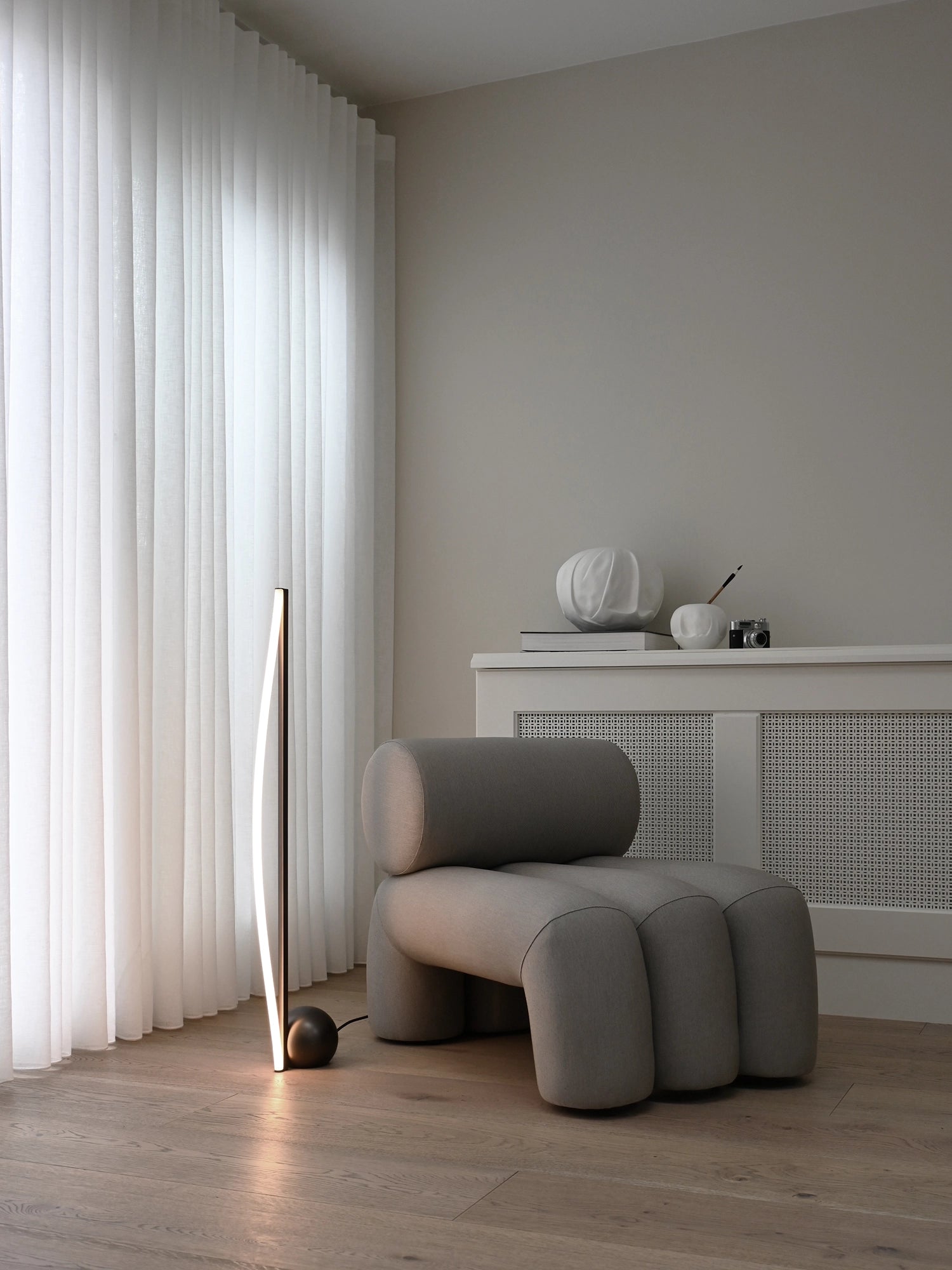101 CPH Bow Floor Lamp, a modern black metal LED strip with a gracefully curved stem and spherical base, displayed in a light-filled living room. This luxury lamp offers ambient lighting for contemporary spaces.