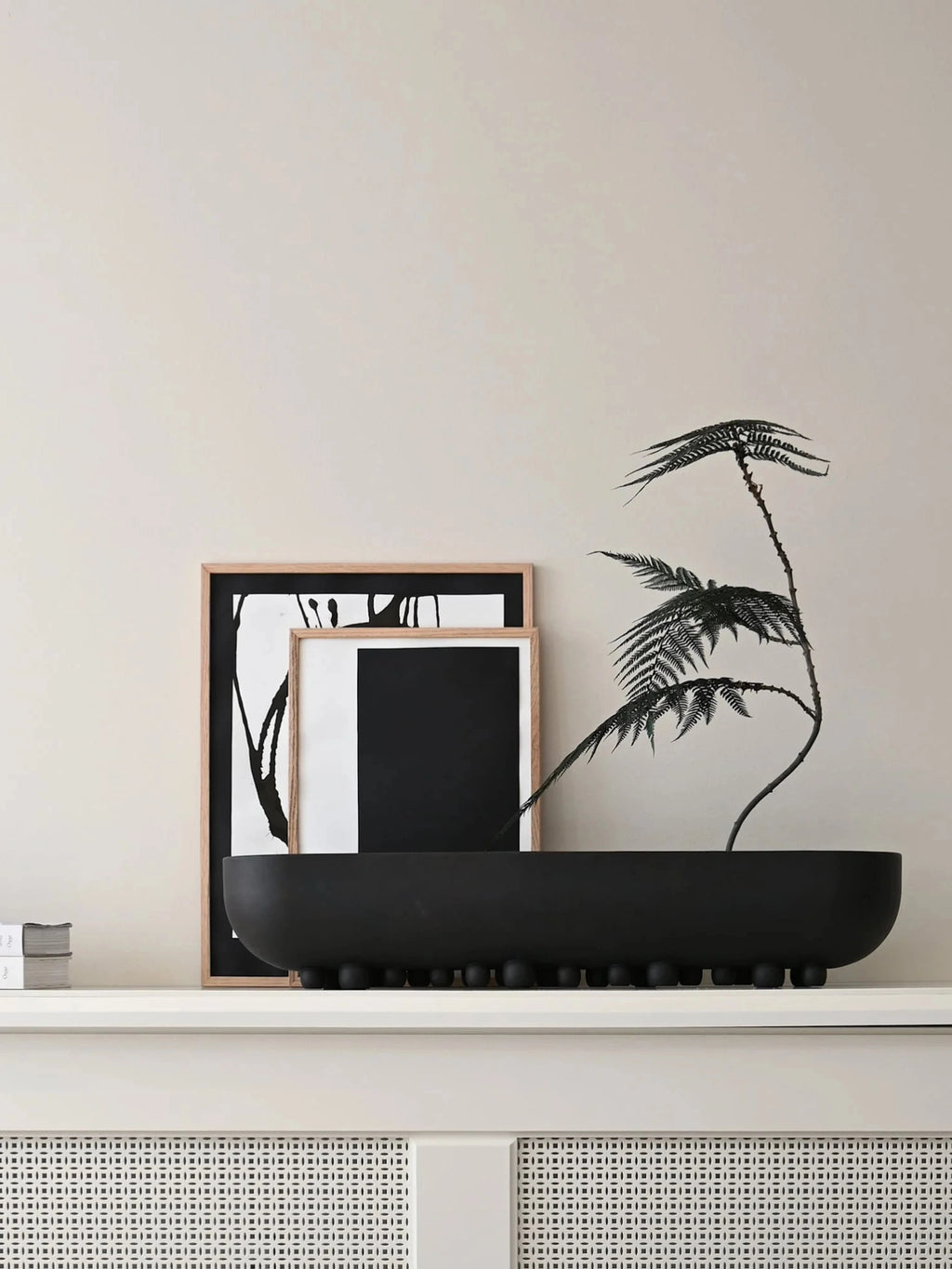 101 CPH Shinju Tray, a sleek black matte ceramic oval tray with spherical feet, styled on a white shelf with vibrant green fern plants and framed abstract art. A premium decorative accent.