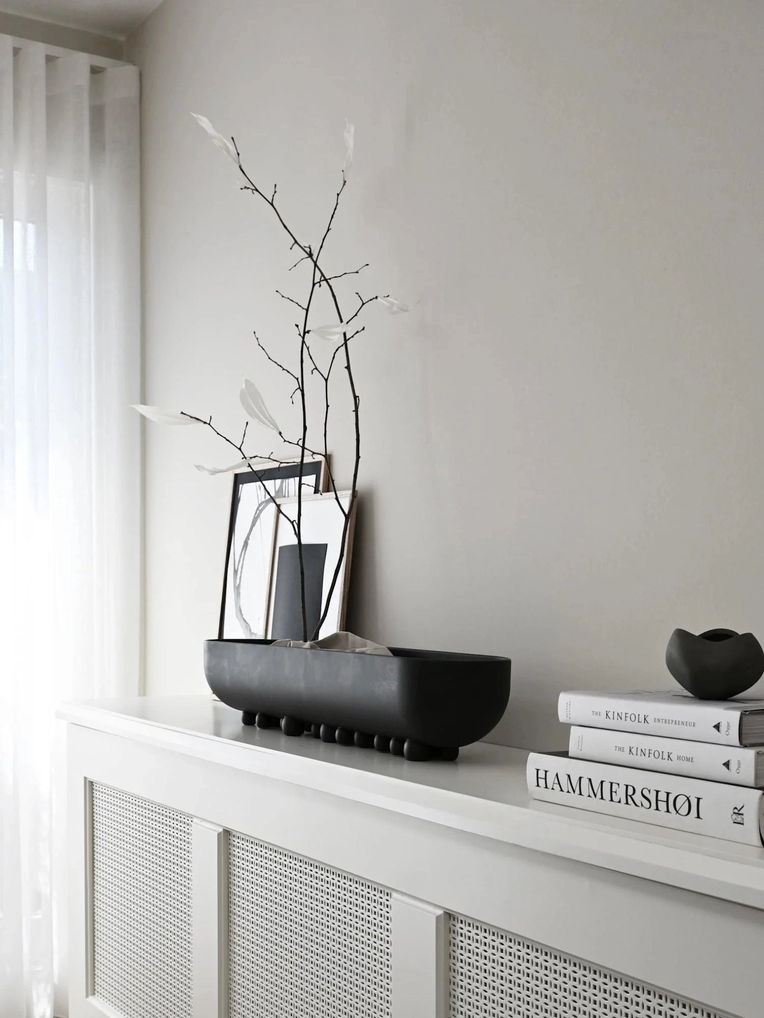 101 CPH Shinju Tray, a long, deep matte black ceramic decorative tray with smooth sides and bulbous feet, styled with branches and art, displayed on a sleek white console. A sculptural, premium home decor piece.