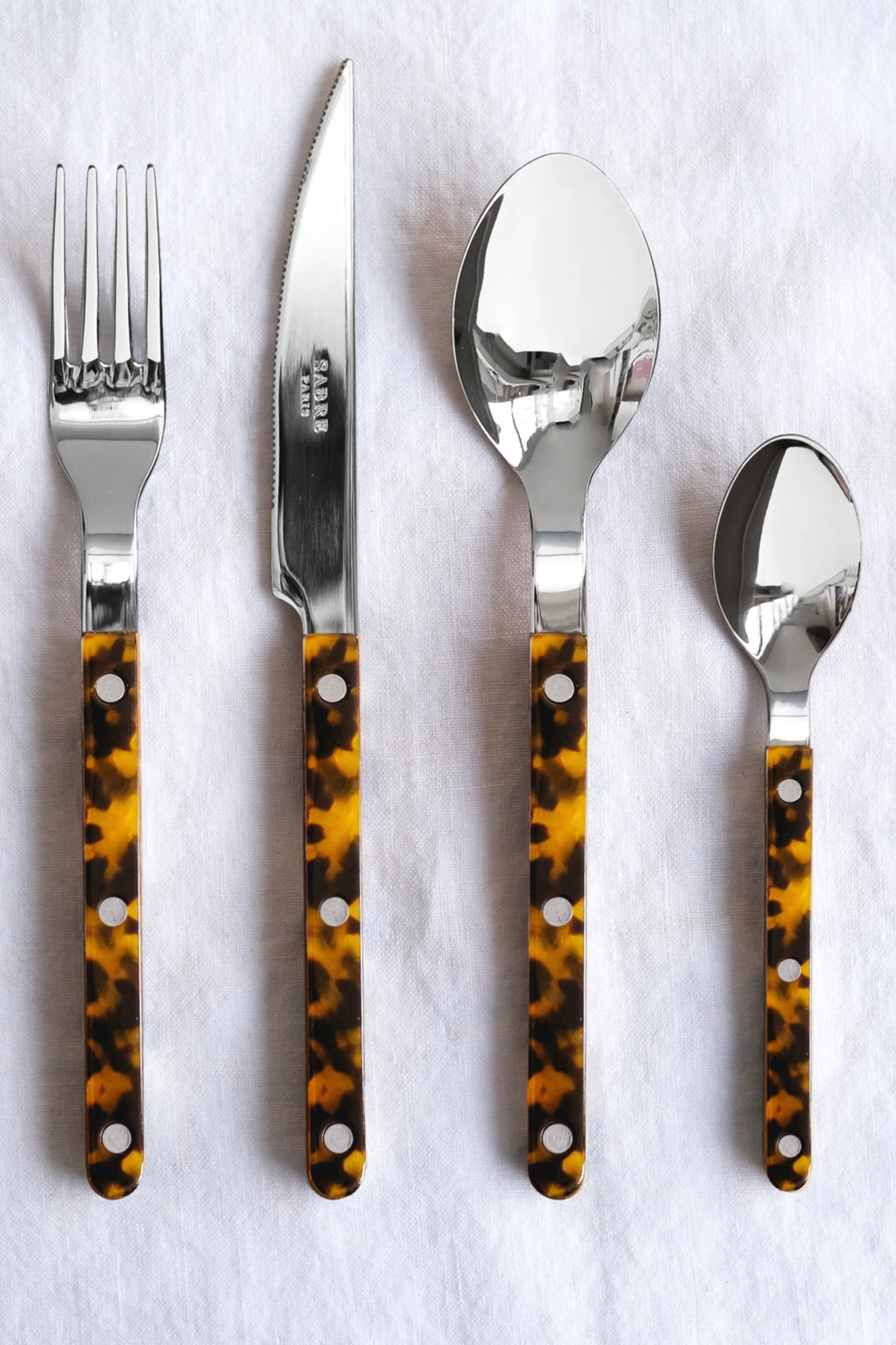 Sabre Paris Bistrot Tortoise 5-Piece Cutlery Flatware Set, featuring polished stainless steel heads and elegant, glossy tortoise shell pattern handles with silver rivets. This stylish and durable cutlery set is perfect for enhancing everyday dining or special occasions for design-conscious individuals.