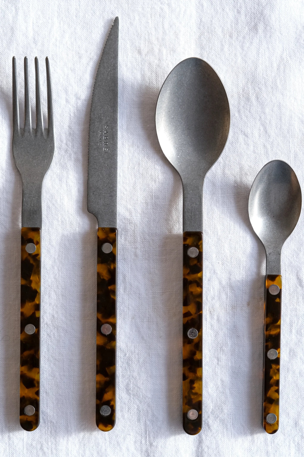 Sabre Paris Bistrot Vintage Tortoise 5-Piece Cutlery Flatware Set, featuring rustic, brushed stainless steel utensils with elegant, mottled tortoise shell-patterned handles secured by silver rivets. This stylish flatware is perfect for adding a touch of vintage charm to everyday dining or special occasions for design-conscious individuals.