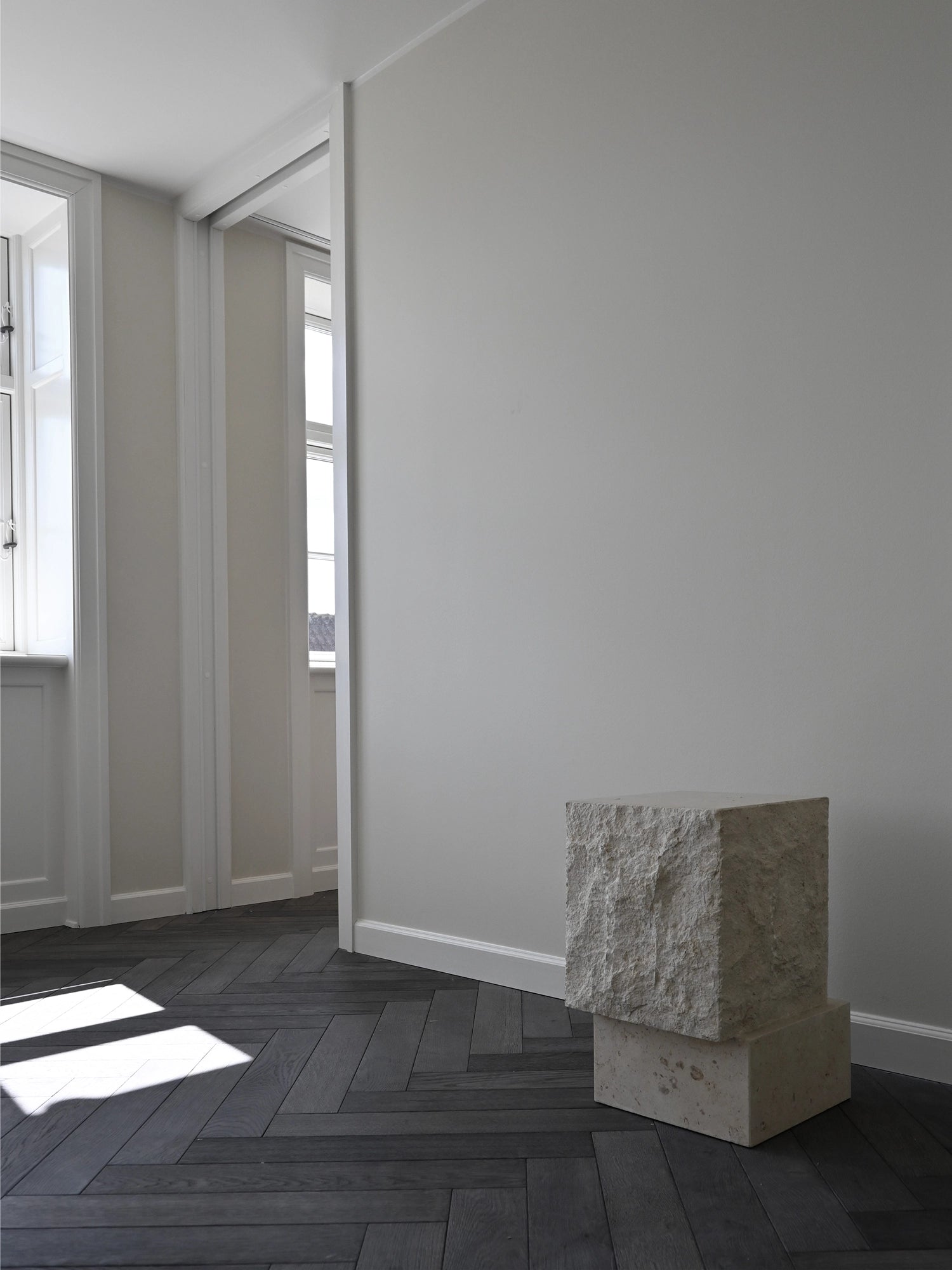 101 CPH Temple Side Table, showcasing two stacked, rough-hewn natural stone blocks with textured, irregular surfaces in an off-white/beige tone on dark herringbone flooring. This luxury sculptural piece is perfect for modern interior decor.