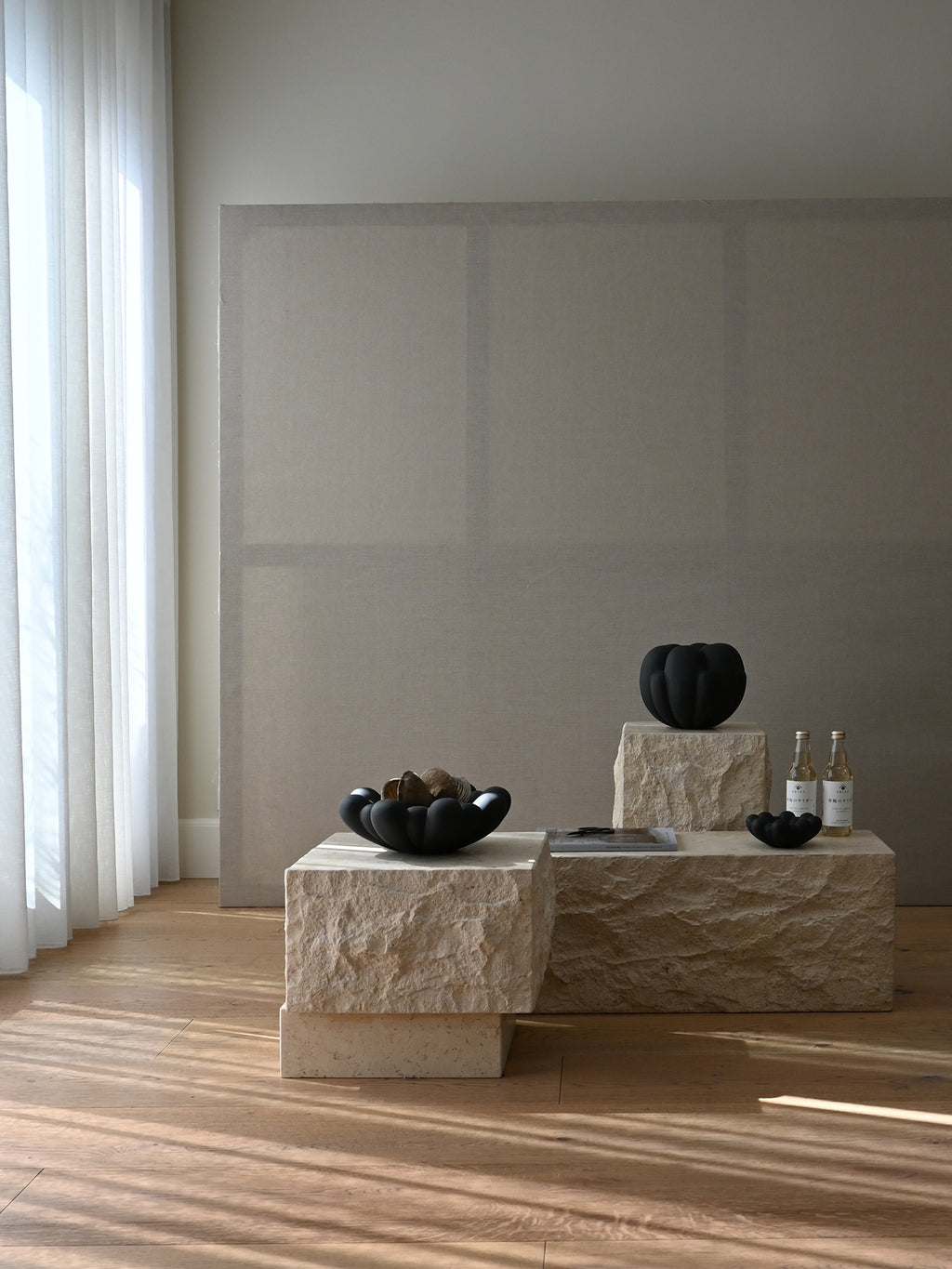 101 CPH Temple Coffee Table: Natural cream travertine blocks form this sturdy, raw stone coffee table, styled with black decorative objects in a sunny room. A luxury focal point for modern living spaces.