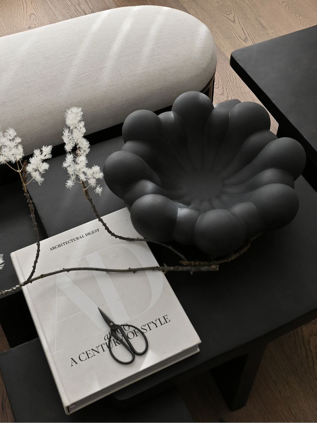 101 CPH Bloom Tray in matte dark grey ceramic, featuring a unique wavy, sculpted design, displayed lifestyle on a black coffee table with a book. A premium decorative homeware piece.