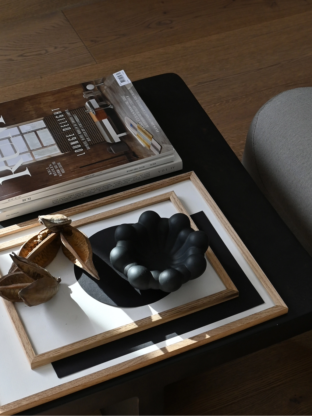 101 CPH Bloom Tray in matte black. The elegant, sculptural bloom-shaped decorative tray is styled on a wooden-framed art print beside magazines and dried botanical pods. A unique accent for modern home decor.