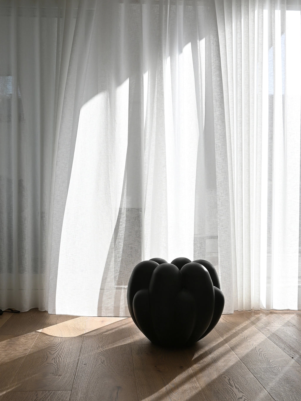 101 CPH Bloom Vase in matte black ceramic, featuring a unique sculptural, organic shape with bulbous, connected forms. Styled on a light wood floor with sheer white curtains in a bright, modern setting. A premium statement piece for contemporary home decor.