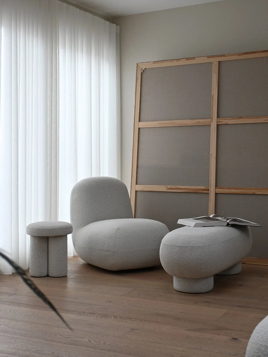 101 CPH Petit Big Foot Bench - Boucle. A light gray, soft textured boucle fabric bench with thick, rounded legs, styled with a book on top, in a modern living space with light wood flooring. Premium accent furniture.