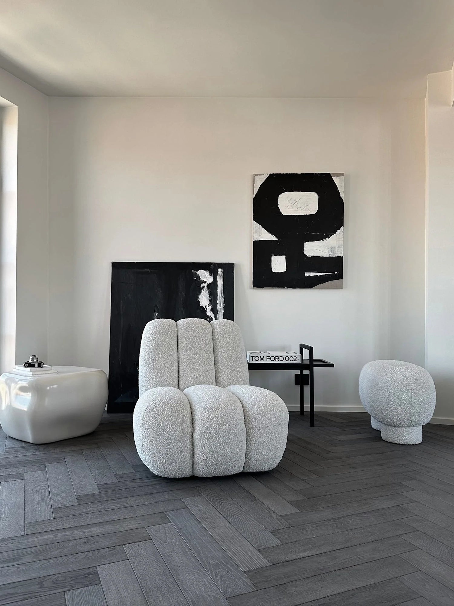 101 CPH Petit Big Foot Bench - Boucle in a minimalist setting. This luxurious, white textured boucle armchair features a distinctive, rounded, plump design, complementing the elegant dark herringbone floor. Ideal for contemporary living spaces.