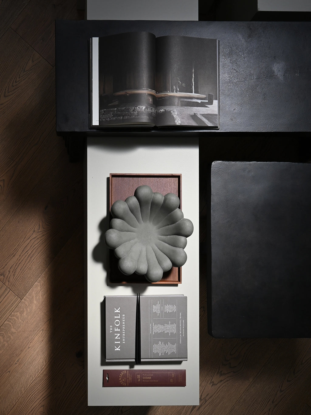 101 CPH Bloom Tray in light grey ceramic with a unique sculptural, flower-like design sits on a dark wooden tray on a white surface, next to books. This premium, handcrafted decorative piece is ideal for modern home decor.