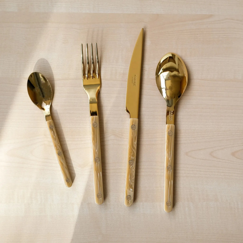 Sabre Paris Bistrot Horn Cutlery Set, featuring luxurious gold-toned stainless steel utensils with elegant cream and beige marbled horn-effect handles. This stylish flatware is perfect for elevating everyday dining or special occasions for design-conscious individuals.