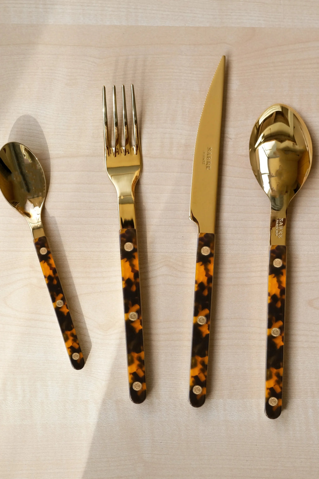 Sabre Paris Bistrot Gold Tortoise 5-Piece Cutlery Flatware Set, featuring polished gold stainless steel utensils and stylish tortoise shell acrylic handles with brass rivets. This elegant flatware is perfect for elevating everyday meals or special occasions for design-conscious hosts.