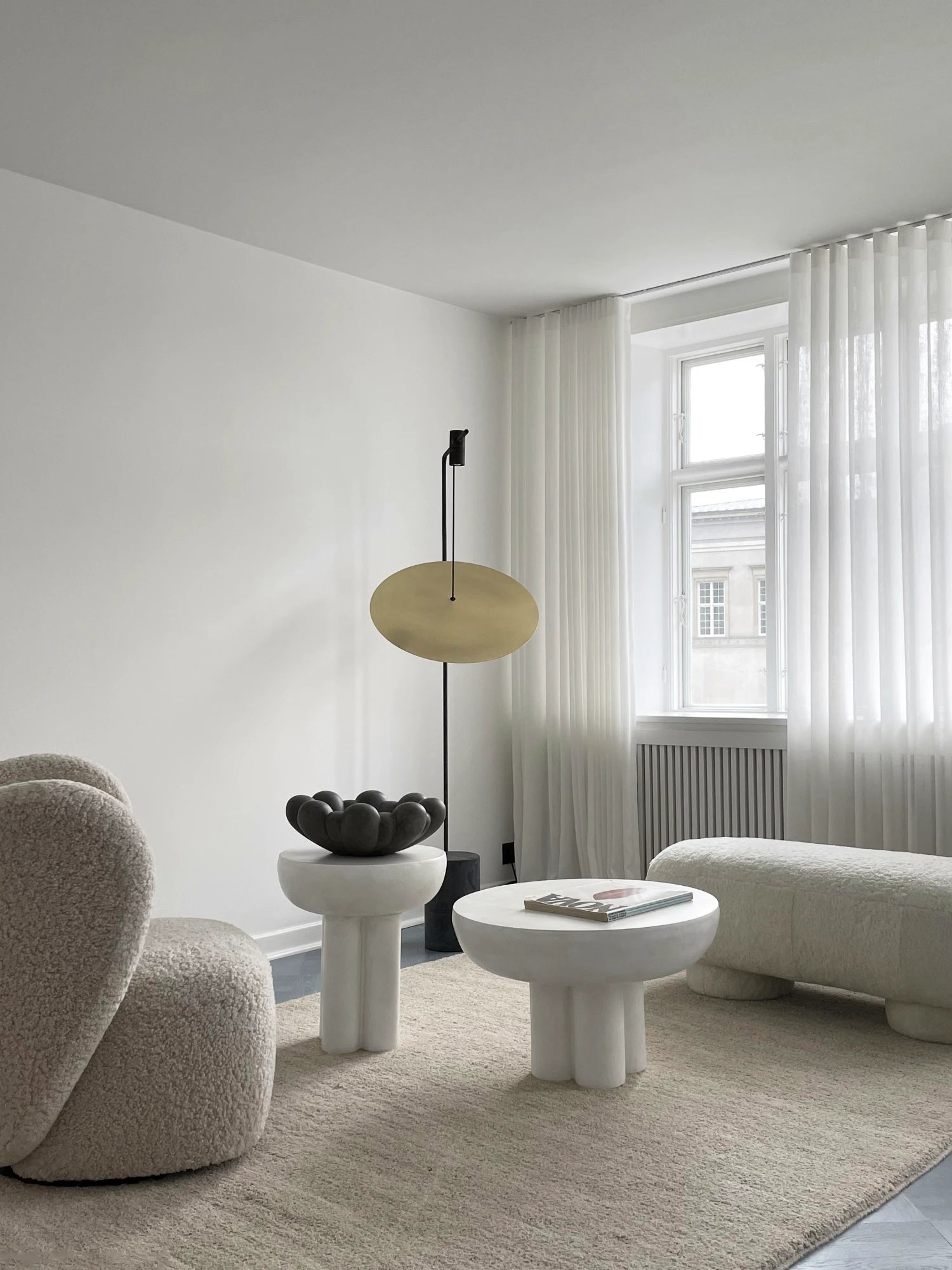 101 CPH Crown Side Table. A luxurious off-white cylindrical pedestal-style accent table features a domed top and three thick, rounded legs in a modern living space. This premium piece complements contemporary interiors.