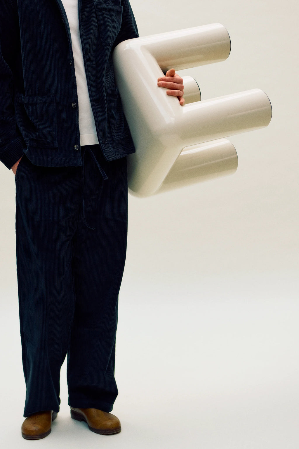 Person holding a large white stool against a plain background